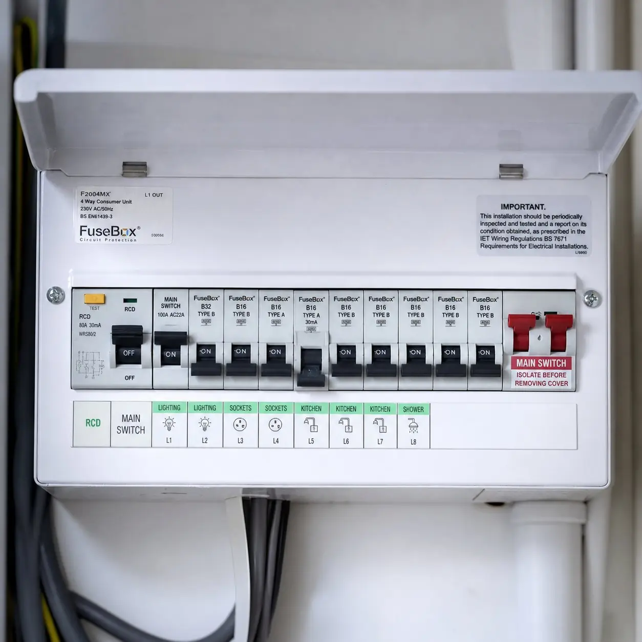 UK consumer unit with the cover open, showing labelled MCBs for lighting, sockets, kitchen and shower circuits with one breaker in the off position